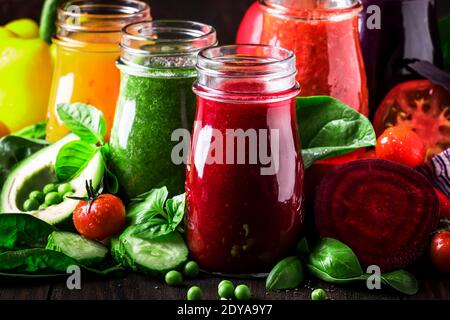 Bunte vegane Gemüsesäfte und Smoothies aus Tomaten, Karotten, Pfeffer, Kohl, Spinat, Rote Bete in Glasflaschen auf rustikalem Küchentisch, ve Stockfoto