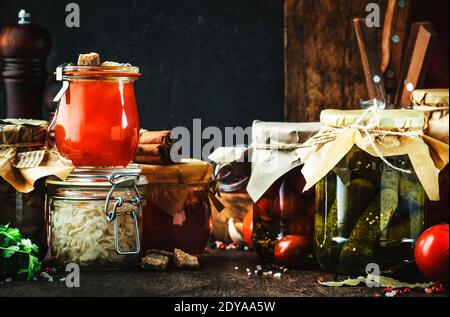 Konzept für Konserven. Fermentierte, eingelegte, marinierte vegetarische Speisen. Bio-Gemüse und Obst in Gläsern mit Gewürzen und Kräutern auf schwarzem Kitc Stockfoto