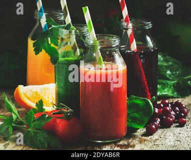 Speisen und Getränke, Auswahl an Gemüse- und Fruchtsäften und Smoothies in Glasflaschen mit Zutaten, auf rustikalem Holztisch, selektiver Fokus Stockfoto