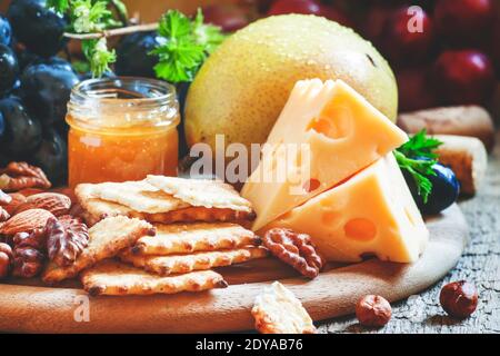 Snack-Teller: Trauben, Birnen, Haselnüsse, Mandeln, Walnüsse, Käse Maasdam und Honig, selektive Fokus Stockfoto