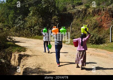 Ooty, Tamil Nadu, Indien - Januar 2017: Gruppe von Menschen, die Trinkwasser in schweren Flaschen in einem kleinen Bergdorf transportieren. Stockfoto