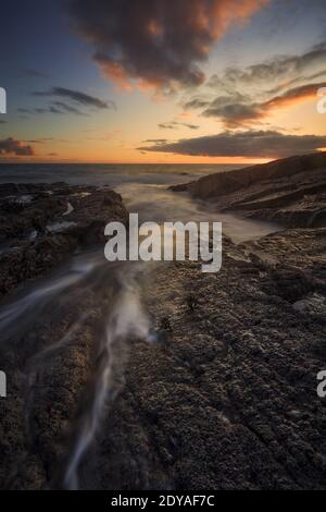 Felsen am Cooper Coast Strand, Waterford, Irland. Sonnenuntergang oder Sonnenaufgang mit seidigem Wasser. UNESCO-geschützte Küste Stockfoto