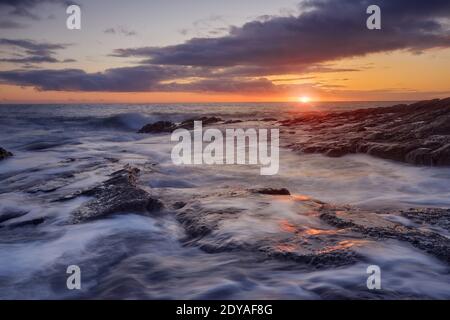Felsen am Cooper Coast Strand, Waterford, Irland. Sonnenuntergang oder Sonnenaufgang mit seidigem Wasser. UNESCO-geschützte Küste Stockfoto