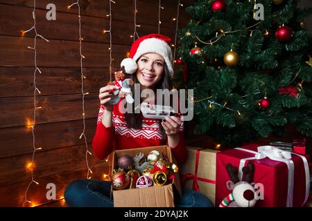 Lächelnde junge Frau in Santa Hut setzen Dekorationen auf Weihnachten Baum zu Hause Stockfoto