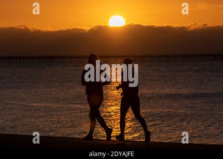 Southend on Sea, Essex, Großbritannien. Dezember 2020. Der Weihnachtstag in Southend ist kalt, aber hell angebrochen, mit Temperaturen knapp über dem Gefrierpunkt. Jogger laufen bei Sonnenaufgang entlang der Promenaden. Zwei Lauferinnen joggen am Meer entlang, wenn die Sonne aufgeht Stockfoto