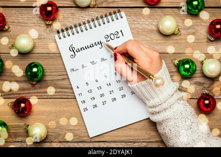 Weibliche Hand hält Stift, offenen Kalender Januar 2021, Weihnachtsdekor auf Holztisch Draufsicht Flat Lay Bildung, Ziele, Vorsätze, Plan, kleiner Besitzer Stockfoto