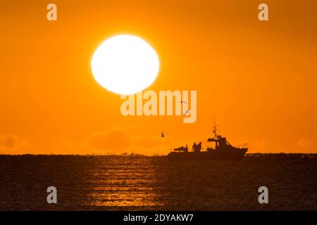 Mudeford, Dorset, Großbritannien. Dezember 2020. Wetter in Großbritannien. Ein Fischerboot wurde an einem kalten, klaren, sonnigen Morgen am Weihnachtstag gegen den goldenen Sonnenaufgang vom Avon Beach in Mudeford in Dorset geschilhoutet. Bild: Graham Hunt/Alamy Live News Stockfoto