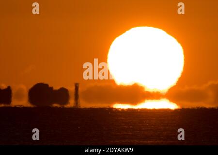 Mudeford, Dorset, Großbritannien. Dezember 2020. Wetter in Großbritannien. Die Sonne geht von hinter den Needles auf der Isle of Wight auf, von Avon Beach in Mudeford in Dorset an einem kalten, klaren sonnigen Morgen am Weihnachtstag betrachtet. Bild: Graham Hunt/Alamy Live News Stockfoto