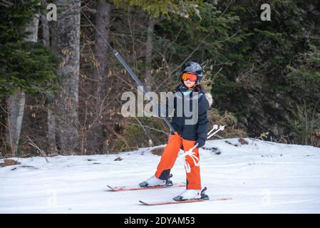 Skifahren im Schnee. Ein asiatisches Mädchen, das auf dem Skilift sitzt, indem es das Seil ergreifet und Skistöcke hält. Urlaub in der Schweiz. Glückliche Kindheit, Stockfoto