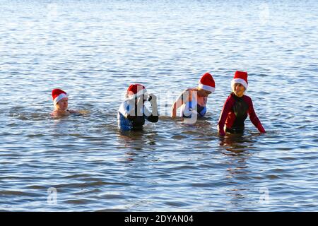 Mudeford, Dorset, Großbritannien. Dezember 2020. Wetter in Großbritannien. Schwimmer in festlichen Weihnachtsmützen genießen ein frühes Bad im Meer am Avon Beach in Mudeford in Dorset an einem kalten, klaren sonnigen Morgen am Weihnachtstag. Bild: Graham Hunt/Alamy Live News Stockfoto