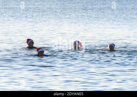 Mudeford, Dorset, Großbritannien. Dezember 2020. Wetter in Großbritannien. Schwimmer in festlichen Weihnachtsmützen genießen ein frühes Bad im Meer am Avon Beach in Mudeford in Dorset an einem kalten, klaren sonnigen Morgen am Weihnachtstag. Bild: Graham Hunt/Alamy Live News Stockfoto