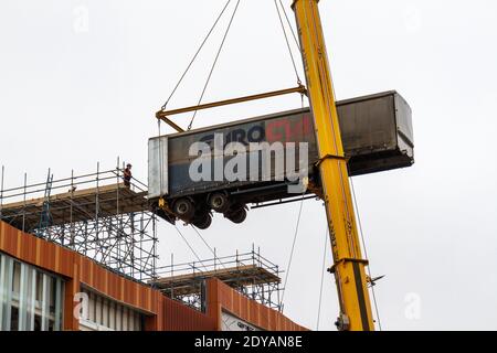 Ein mobiler Kran, der den Anhänger eines Sattelschleppers auf eine Rampe hoch oben auf einem Gebäude im Bau in Nottingham, Notts, Großbritannien, hebt. Stockfoto