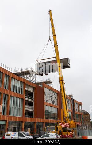 Ein mobiler Kran, der den Anhänger eines Sattelschleppers auf eine Rampe hoch oben auf einem Gebäude im Bau in Nottingham, Notts, Großbritannien, hebt. Stockfoto