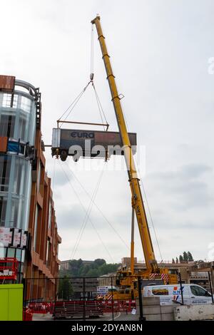 Ein mobiler Kran, der den Anhänger eines Sattelschleppers auf eine Rampe hoch oben auf einem Gebäude im Bau in Nottingham, Notts, Großbritannien, hebt. Stockfoto