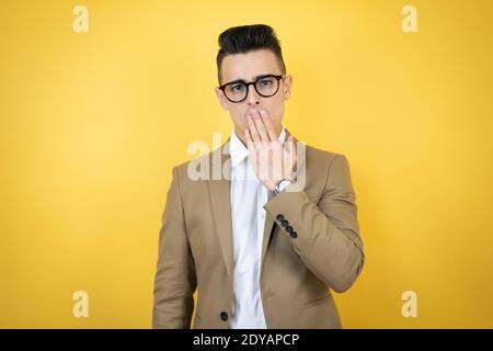 Junge Geschäftsmann über isoliert gelben Hintergrund überrascht, die Abdeckung Mund mit der Hand Stockfoto