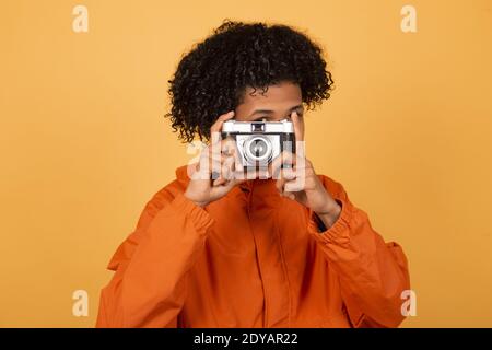 Ein junger afroamerikanischer Mann in einem orangen Regenmantel mit Eine Retro-Fotokamera Stockfoto