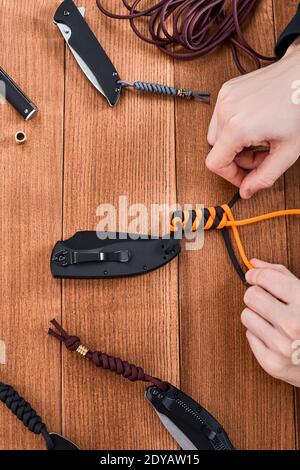 Draufsicht auf die Hände, die ein Paracord Lanyard mit schwarz machen Und orangefarbene Seile Stockfoto