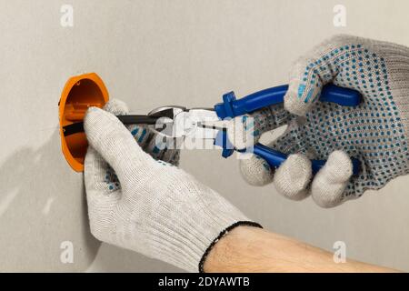 Die Hände des Elektrikers reinigen die Isolierung der elektrischen Leitungen mit Drahtschneider Stockfoto