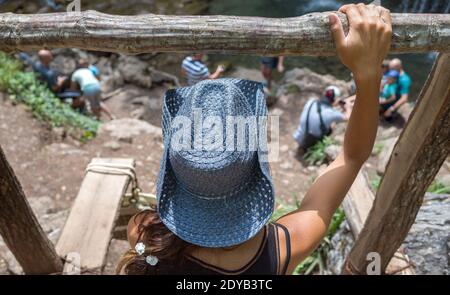 Ein junges Mädchen in einem blauen Strohhut sitzt auf einer Holzbrücke. Stockfoto