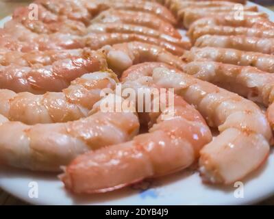 Gekochte und geschälte ganze Garnelen auf einem weißen Teller zusammen gelegt. Typische Meeresfrüchte zum Mittag- und Abendessen zu Weihnachten. Horizontale Fotografie. Stockfoto