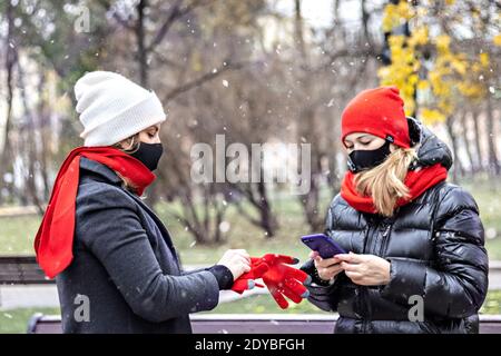 Zwei junge Frauen mit medizinischen Schutzmasken treffen sich in einem Herbstpark. Soziale Distanz und Isolation während der Coronavirus-Pandemie.man trägt Handschuh Stockfoto
