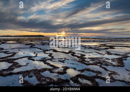 Ein schöner Sonnenuntergang über dem Meer mit felsigen Strand und Gezeitenbecken im Vordergrund Stockfoto