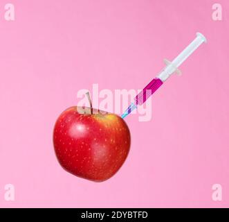 Genetisch modifizierter roter Apfel mit Spritzen auf rosa Hintergrund.Medizinische Spritze Einspritzung von GVO in Apfel Stockfoto