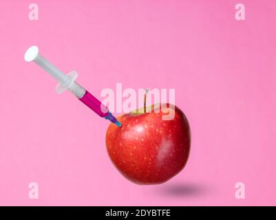 Genetisch modifizierter roter Apfel mit Spritzen auf rosa Hintergrund.Medizinische Spritze, die GVO in Apfel injiziert, Fruchtkonzept minimal Stockfoto