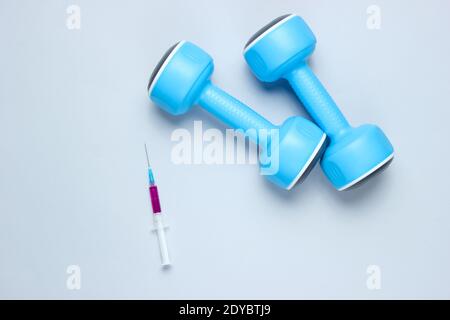 Doping im Sport. Anabole Steroide. Sportapotheke. Blaue Kunststoff-Kurzhanteln, Spritze auf grauem Hintergrund. Draufsicht. Stockfoto