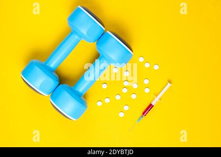 Doping im Sport. Anabole Steroide. Sportapotheke. Kunststoff-Hanteln, Spritze, Pillen auf gelbem Hintergrund. Draufsicht. Stockfoto