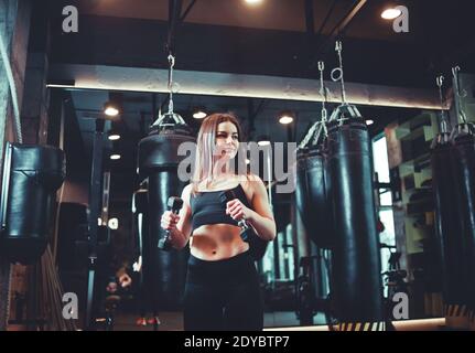 Attraktive athletische Mädchen in Sportswear hält Hanteln in den Händen und trainiert Bizeps im Boxstudio. Stockfoto