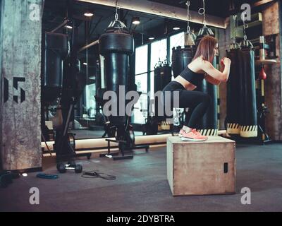 Fitness Frau springen auf Holzkiste Training in der Turnhalle, Training. Brunette Mädchen in der Sportbekleidung tun einige springen Übungen im Fitnessstudio Stockfoto