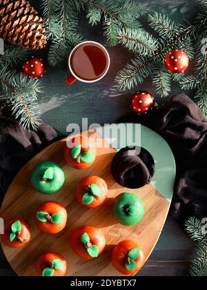 Marzipan Schwamm Äpfel. Weihnachtsdessert, flach auf Holzbrett gelegt. Tasse Tee, Tannenzweige, grüne Kerze, Kegel. Stockfoto