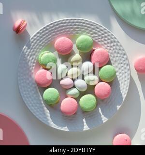 Osterbonbons auf weißem Hintergrund mit langen Schatten. Ostereier aus Marzipan, rosa und mintgrüne Makronen auf weißem Teller. Leckere kreative Dessert in Stockfoto