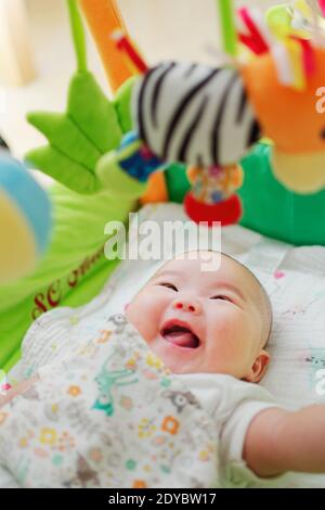 Drei Monate altes chinesisches Baby, das glücklich mit baumelnden Spielsachen über ihrem Bett spielt. Stockfoto
