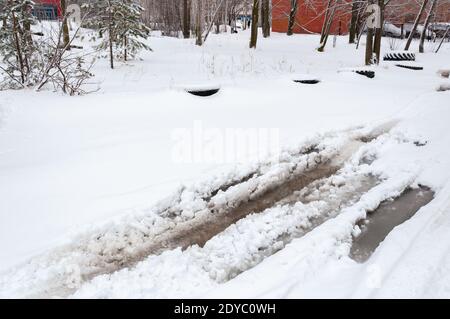 Geschmolzener Schnee auf einer Asphaltfläche mit tiefem Wasser und Schnee an den Rändern. Pfützen auf einer verschneiten Straße im Frühjahr. Stockfoto