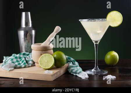 Typisch mexikanischer margarita Cocktail mit Limetten und Cocktailshaker auf schwarzem und grünem Hintergrund auf Holzsockel. Stockfoto