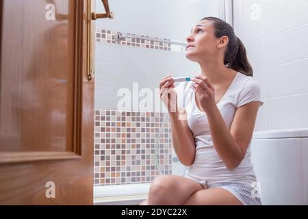 Junge kaukasische Frau, besorgt über Schwangerschaftstest Ergebnisse zu Hause. Frau und Schwangerschaft Tests Konzept. Stockfoto