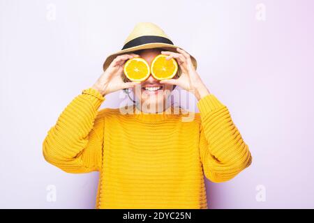 Junge lustige kaukasische Frau, mit gelbem Pullover und mit zwei orangefarbenen Scheiben in den Augen posiert lustig im Fotostudio. Stockfoto