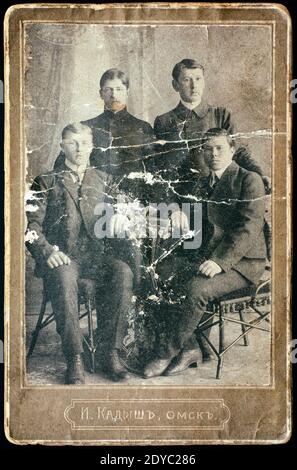 Old Scratch Vintage Foto von vier jungen Männern im Fotostudio. Foto wurde zu Beginn des 20. Jahrhunderts in Omsk aufgenommen. Stockfoto