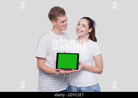 Paar zeigt Tablet Green Screen beobachten einander isoliert stehen. Konzept Für Werbung, Werbung Und Werbung Stockfoto