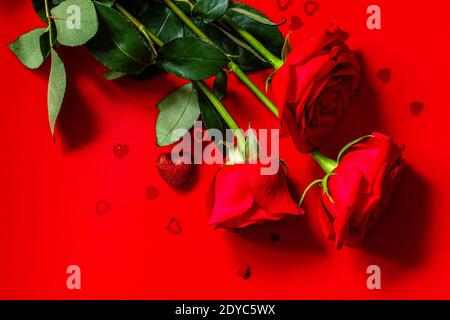 Bouquet von roten Rosen und Dekor in Form eines Herzens auf einem roten Hintergrund. Draufsicht, flach liegend. Speicherplatz kopieren. Stockfoto
