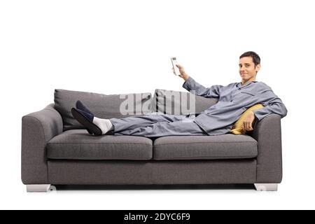 Mann im Pyjama auf einem Sofa liegen und halten ein Fernbedienung über eine Klimaanlage, die auf weißem Hintergrund isoliert ist Stockfoto