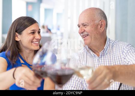 Reifer Mann und junge Frau genießen und lächeln, verbringen Zeit zusammen. Toasting mit einem Glas Wein Stockfoto
