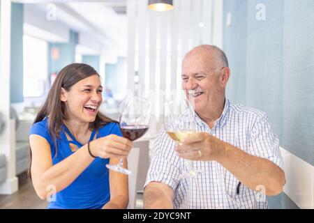 Reifer Mann und junge Frau genießen und lächeln, verbringen Zeit zusammen. Toasting mit einem Glas Wein Stockfoto