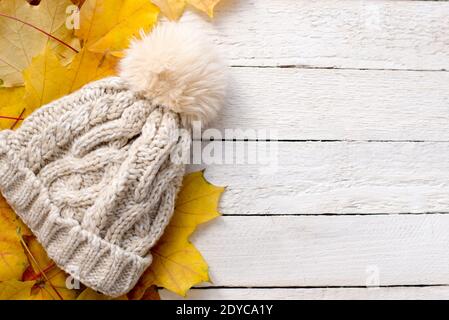 Gestrickter Hut und gelbe Blätter auf weißem Holzhintergrund, Kopierraum. hut mit Pompon Stockfoto
