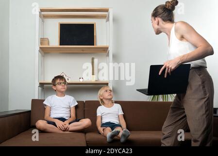 Mama mit Laptop in den Händen und zwei Jungen auf der Couch. Mutter nahm den Kindern den Laptop weg Stockfoto