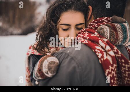 Junge Mann und Frau stehen küssen und umarmen. Braut und Bräutigam in Liebe Paar in gestrickten Schal und Fäustlinge im Winter mit Schnee und Schneeflocken. Hochzeit Stockfoto