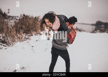 Junger Mann und Frau, die im Schnee liegen und lachen Narren um Spaß zu spielen snowballs.bride und Bräutigam in der Liebe Paar in gestrickten Schal und Stockfoto