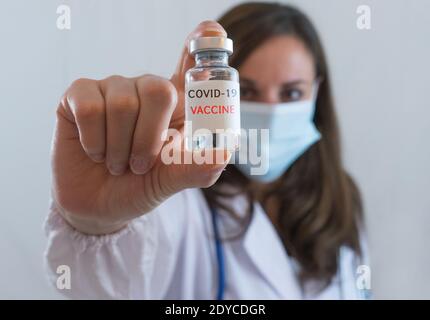 Kaukasische Frau Arzt oder Krankenschwester in Uniform und Handschuhe Tragen Gesichtsmaske schützende im Labor halten Impfstoffflasche und Auf Flasche hat 'COVID-19 VACCI Stockfoto